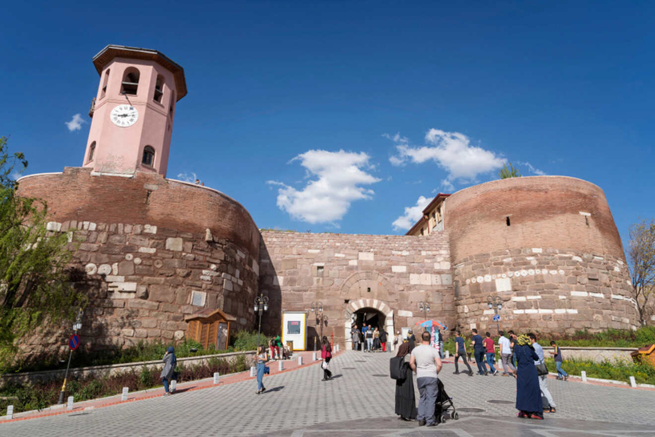 Visitors walking through Ankara Castle's fortified gate, which features a clock tower, revealing the historical architecture of the city's bygone eras