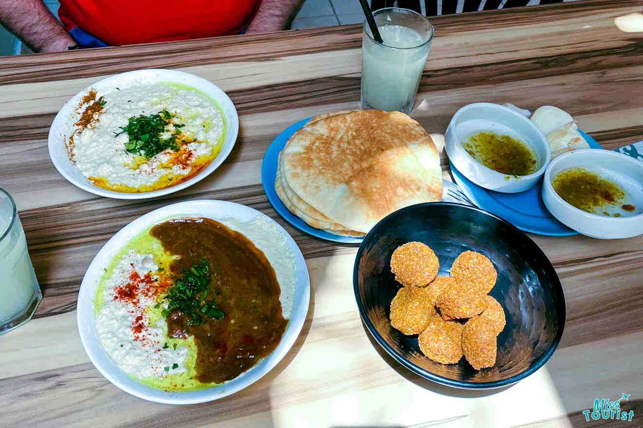 A table full of Middle Eastern dishes, showcasing hummus topped with olive oil and spices, a plate of golden falafel, fluffy pita bread, and small bowls of olive oil for dipping