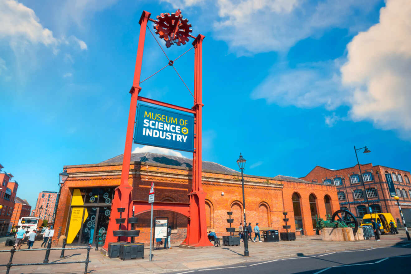 The entrance of the Museum of Science and Industry in Manchester, marked by a distinctive red structure with gears, on a sunny day with clear skies