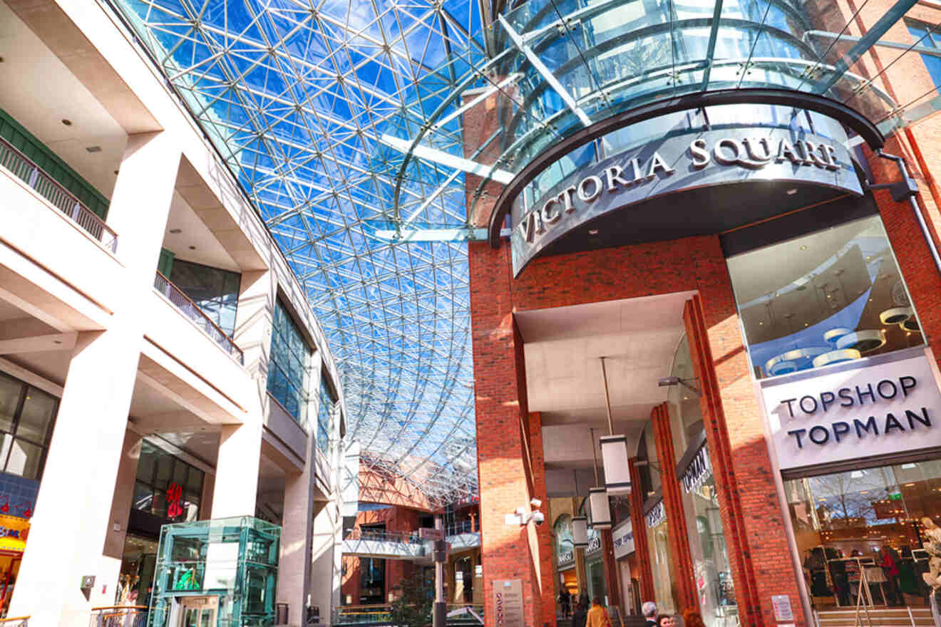 Spacious and bright interior of Victoria Square shopping district in Belfast, showcasing multi-level stores, a glass dome overhead, and shoppers enjoying the facilities