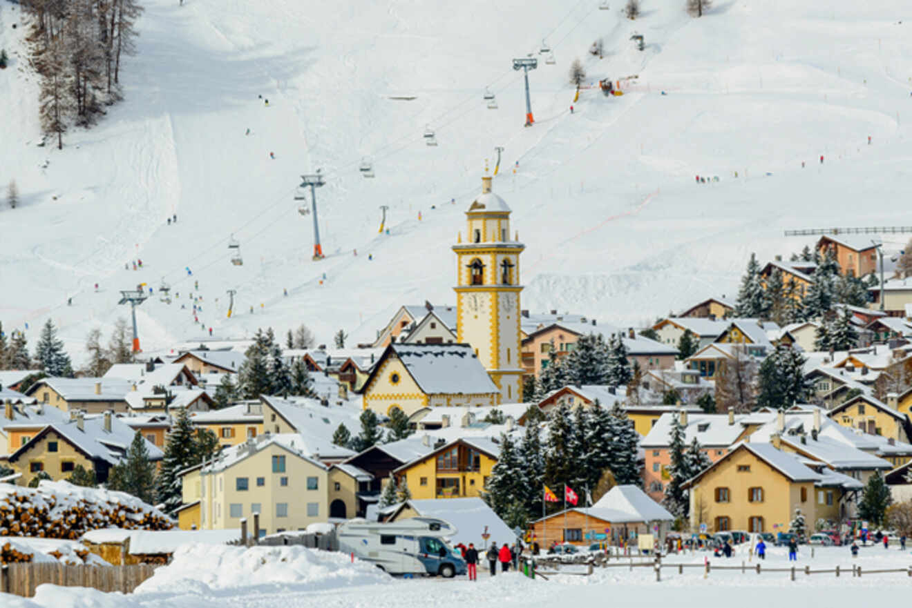 Vibrant ski scene in Celerina-Schlarigna with a striking yellow church tower, surrounded by quaint houses against the backdrop of a bustling ski slope in St. Moritz