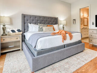 Elegant bedroom with a gray upholstered bed, patterned accent pillows, and warm lighting.