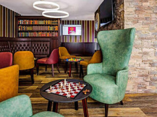 A vibrant hotel lounge with eclectic seating, a bookshelf filled with colorful books, and unique circular lighting fixtures