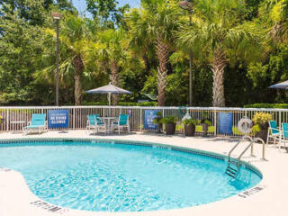 Outdoor pool area at the Holiday Inn Express surrounded by lush palm trees, featuring poolside seating and a clear blue swimming pool