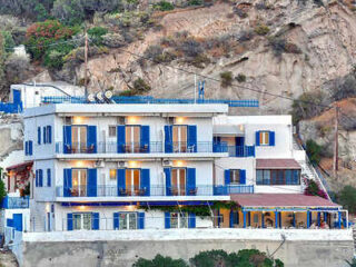 A traditional Greek hotel with blue shutters perched on a hillside