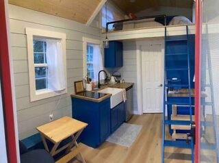 Compact and efficient tiny house interior with blue cabinets, wooden floors, and a loft bed