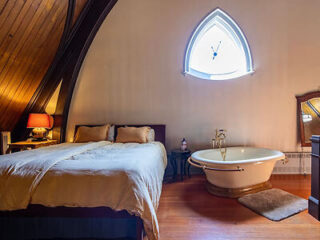 Attic bedroom with gothic window, freestanding bathtub, wooden floors, and a cozy bed
