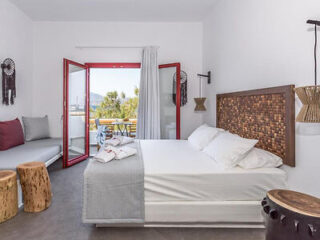A chic, modern bedroom with a large bed, red accents, and a balcony overlooking the Greek landscape