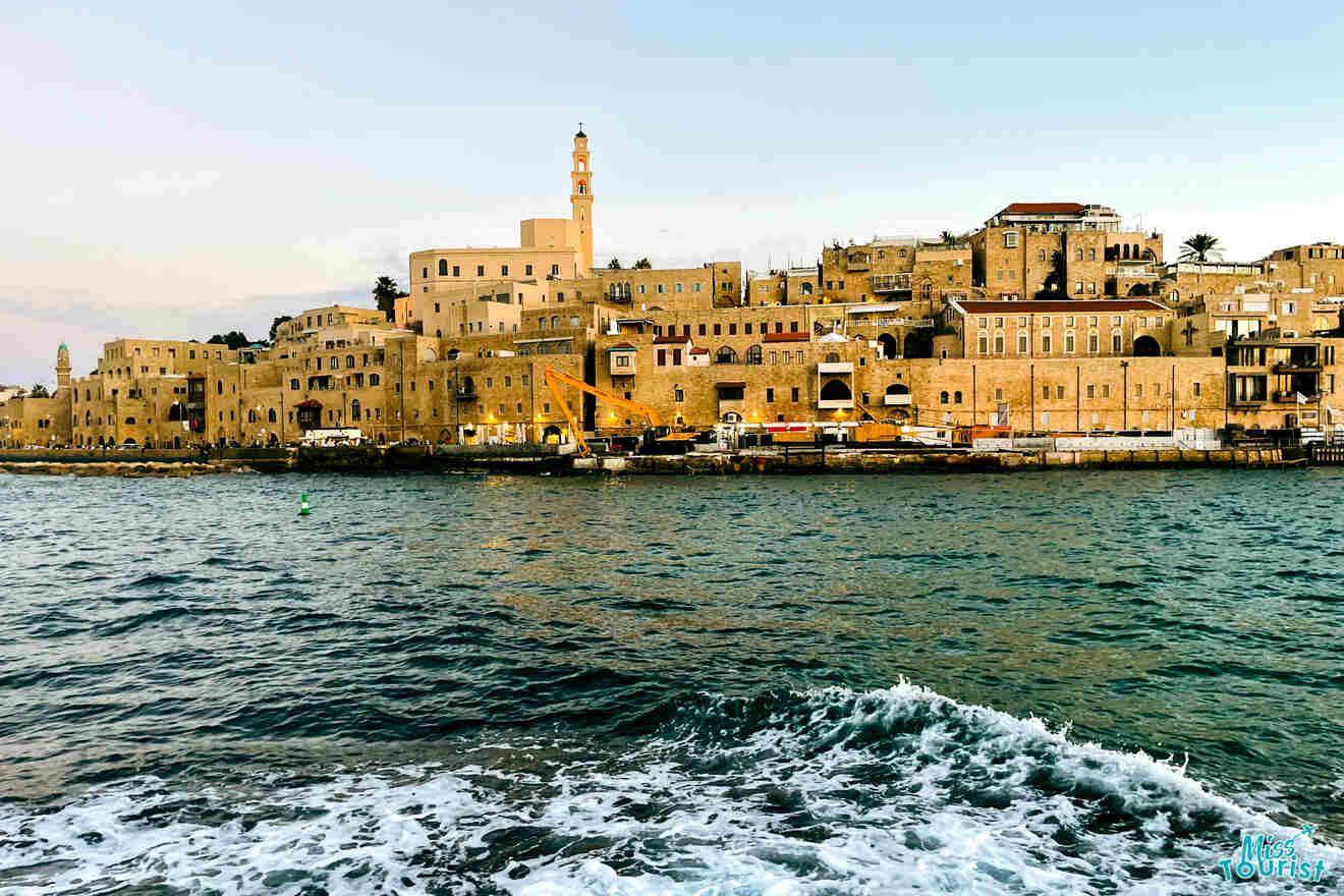 Old coastal town viewed from the sea with historic buildings and minaret at sunset