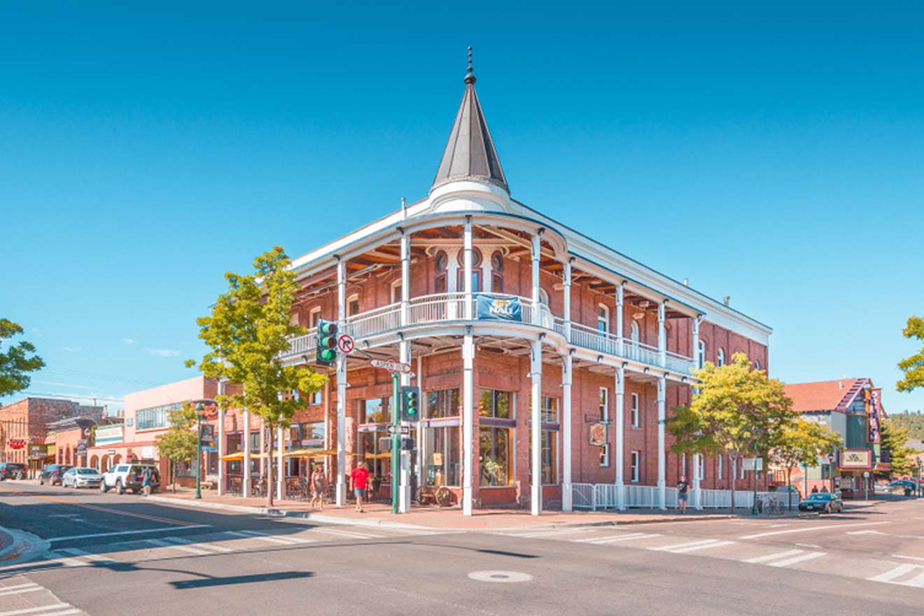 Historic red brick corner building with white-trimmed wraparound balconies under a clear blue sky, situated at a street intersection in a quaint town near the Grand Canyon, conveying a welcoming atmosphere for family stays