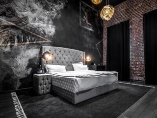 A luxurious bedroom in Black Hotels Köln with an opulent tufted bed, eclectic lighting, exposed brick walls, and a monochromatic, textured wallpaper