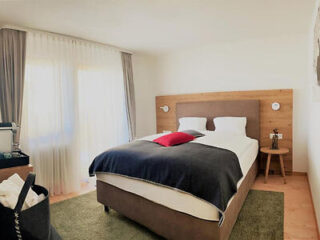 Simplistic hotel room with a large bed, green rug, and natural wood furnishings