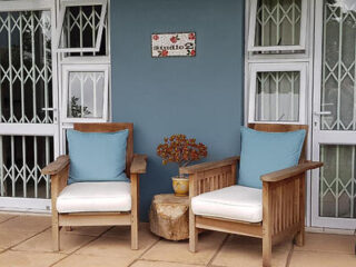 Cozy outdoor seating area at Buckingham Cottage with two wooden armchairs, soft blue cushions, and a serene ambiance
