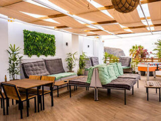 Spacious and modern rooftop lounge area at Ocean Nomads Coworking, with comfortable gray outdoor sofas, wooden tables, and an array of potted plants