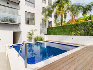 A small but inviting outdoor pool, flanked by wooden decking and lush greenery