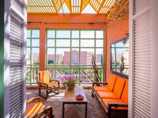 Bright and inviting balcony space with vibrant orange seating, under a lattice pergola, offering a picturesque view of the Marrakech cityscape