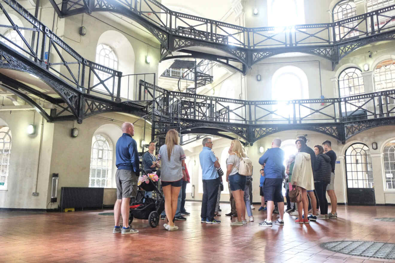 Tour group standing inside the historic Crumlin Road Gaol in Belfast, surrounded by black metal staircases and arched windows, indicative of Victorian-era prison architecture