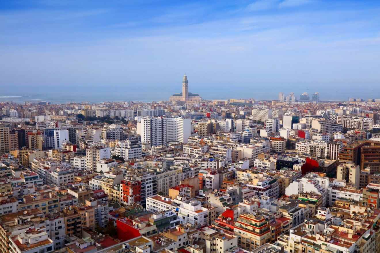Aerial view of Casablanca, Morocco, showcasing the dense urban landscape with a mix of white buildings, city streets, and the historic Hassan II Mosque near the coastline.