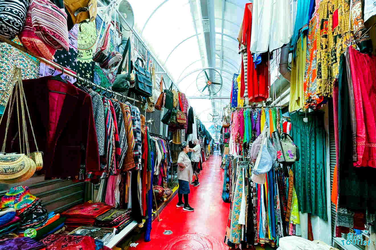 Vibrant and colorful clothing hanging in Jaffa's bustling flea market, with shoppers browsing the eclectic merchandise
