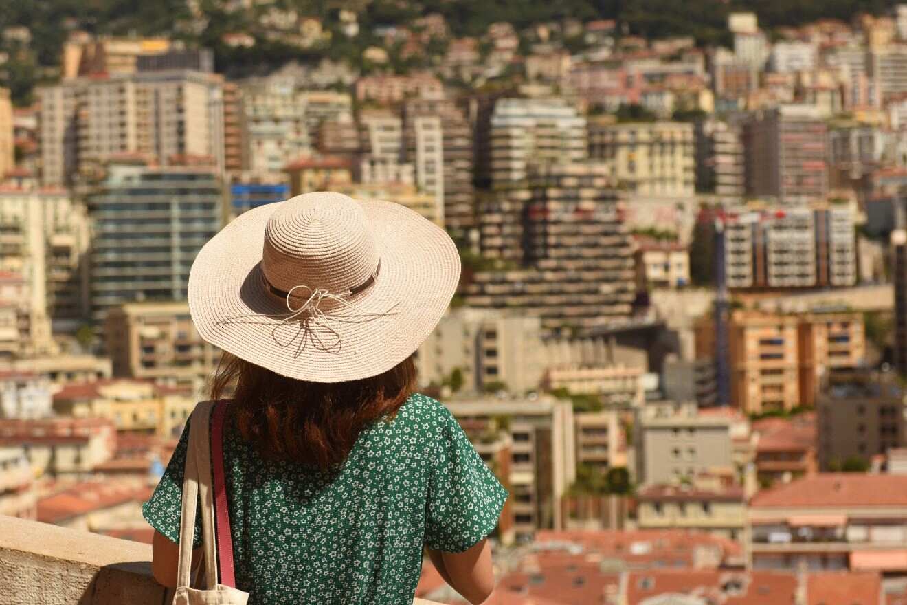 Person with a wide-brimmed hat overlooking a dense residential area of Beausoleil, with a panoramic view of Monaco's buildings in the background