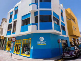 Vibrant blue and yellow exterior of Casa Grande Surf Hostel, standing out on a sunny street corner with welcoming yellow windows and entrance