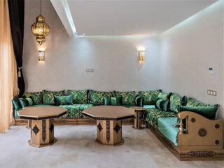 Luxurious Moroccan lounge with plush emerald green sofas and ornate golden tables, illuminated by hanging lanterns casting a warm glow