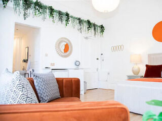 Studio apartment with white decor, orange sofa, and open bed area.