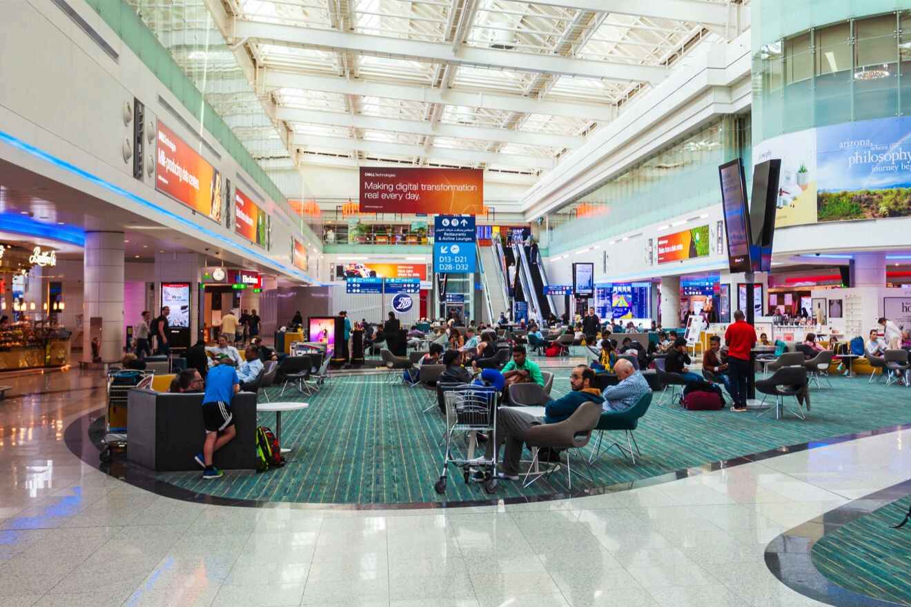 Busy interior of Dubai International Airport with passengers seated and walking, surrounded by shops and digital display boards