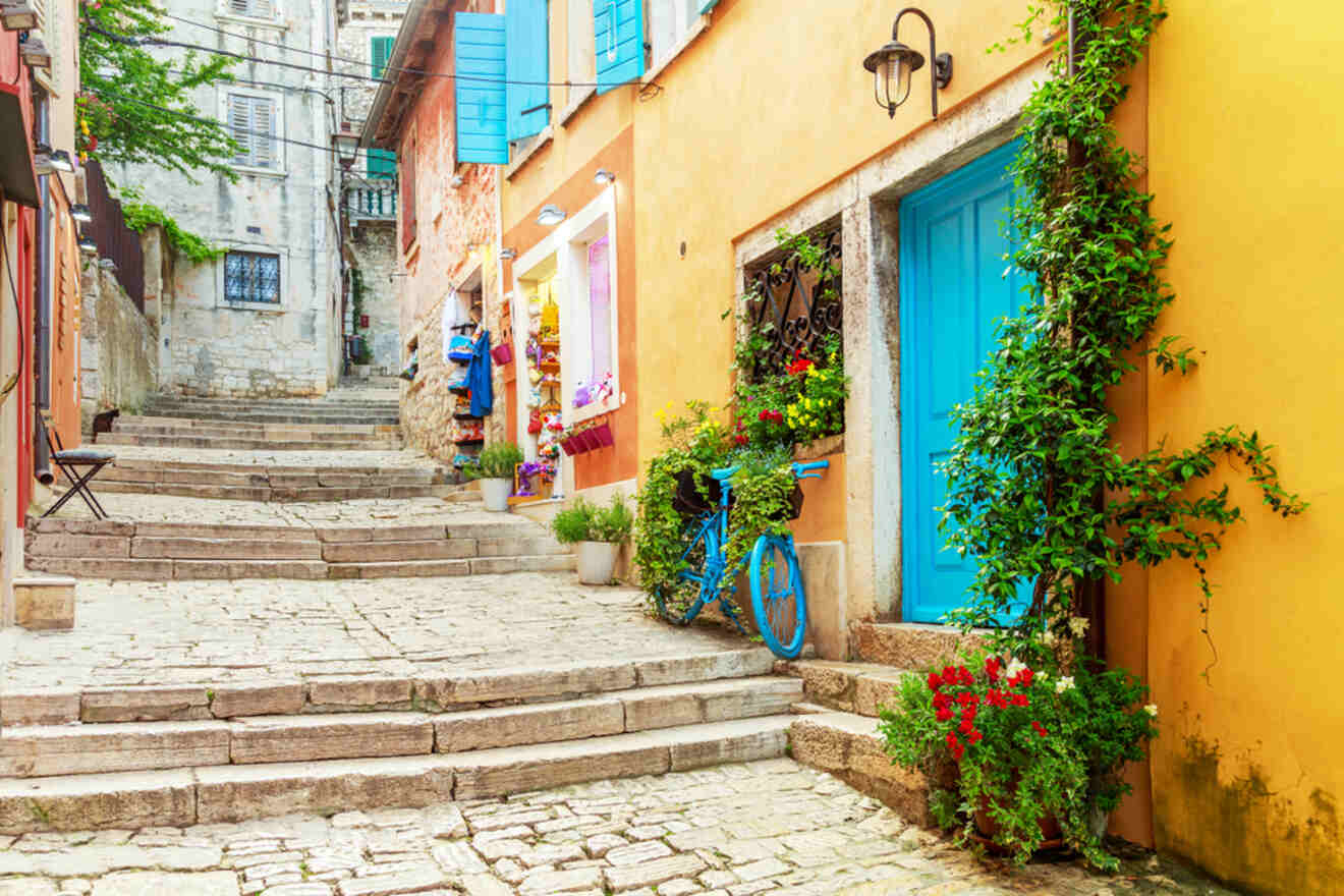 Picturesque stone stairway in Rovinj, flanked by vibrant yellow and blue houses adorned with lush green plants and flowers, exuding a warm Mediterranean ambiance