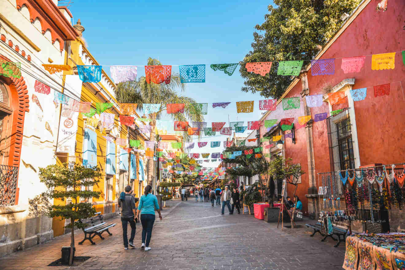 Colorful street scene in Tlaquepaque, Guadalajara, with pedestrians walking under vibrant papel picado banners, showcasing the area's artistic vibe