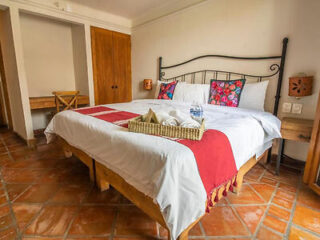 Welcoming hotel room with a large bed, colorful pillows, terracotta-tiled floor