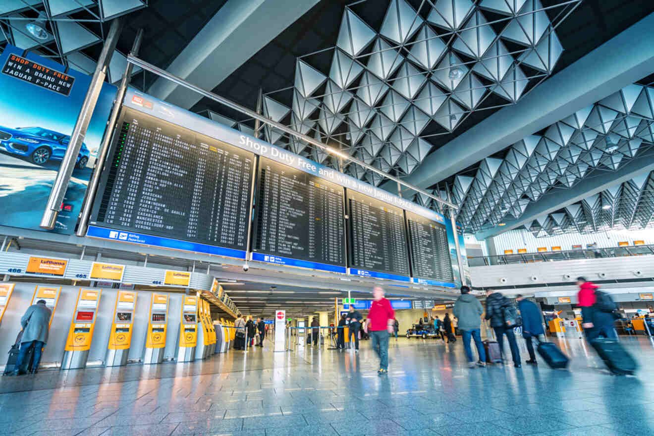Busy interior of Frankfurt Airport with travelers walking past flight information boards, exemplifying a modern travel hub with its iconic geometric ceiling design