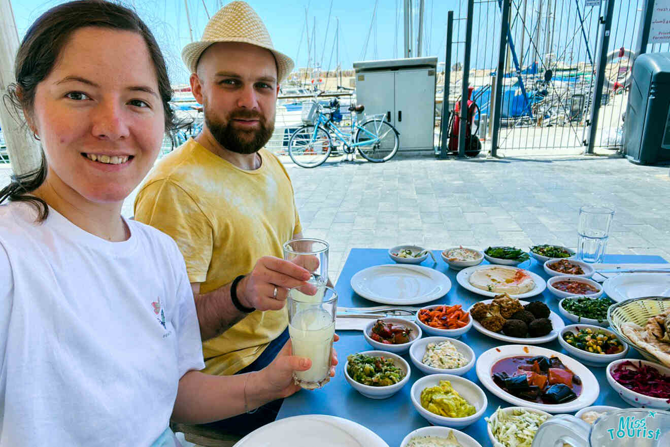 The author of the post with her husband enjoying a variety of Middle Eastern dishes at an outdoor table in Jaffa with a view of the marina