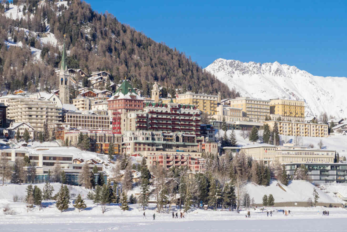 St. Moritz Bad district with luxury hotels and buildings nestled against a backdrop of snowy mountains and a frozen lake with people walking