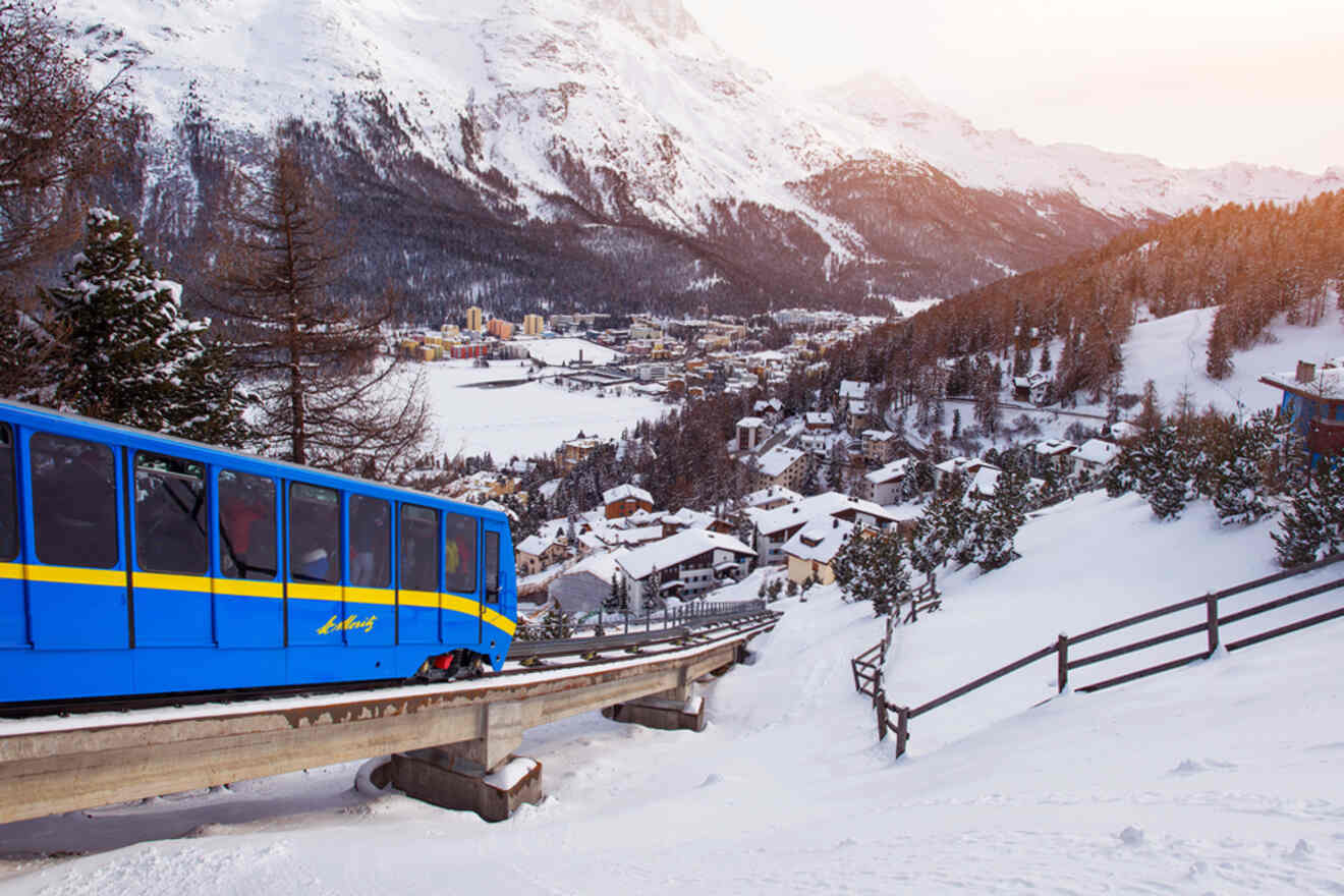 Vibrant blue funicular train ascending the snowy mountainside near St. Moritz with views of the valley and alpine buildings below.