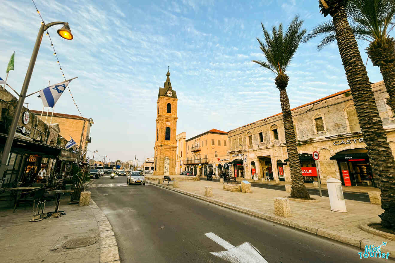 The iconic clock tower of Jaffa standing tall amidst palm trees with the blue sky above and Israeli flags fluttering in the wind