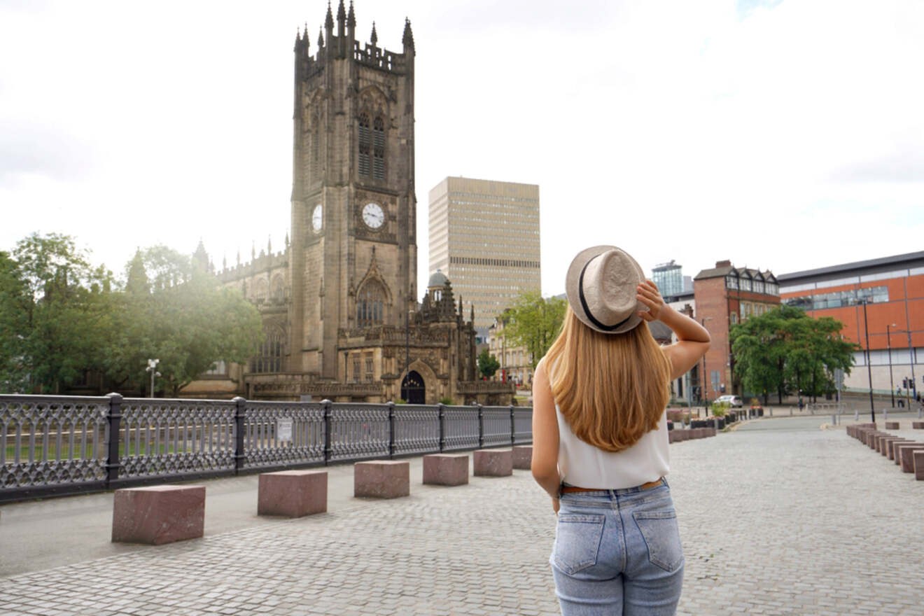 A woman from behind, wearing a hat, looking towards the historic Manchester Cathedral, emphasizing the blend of history and modern city life