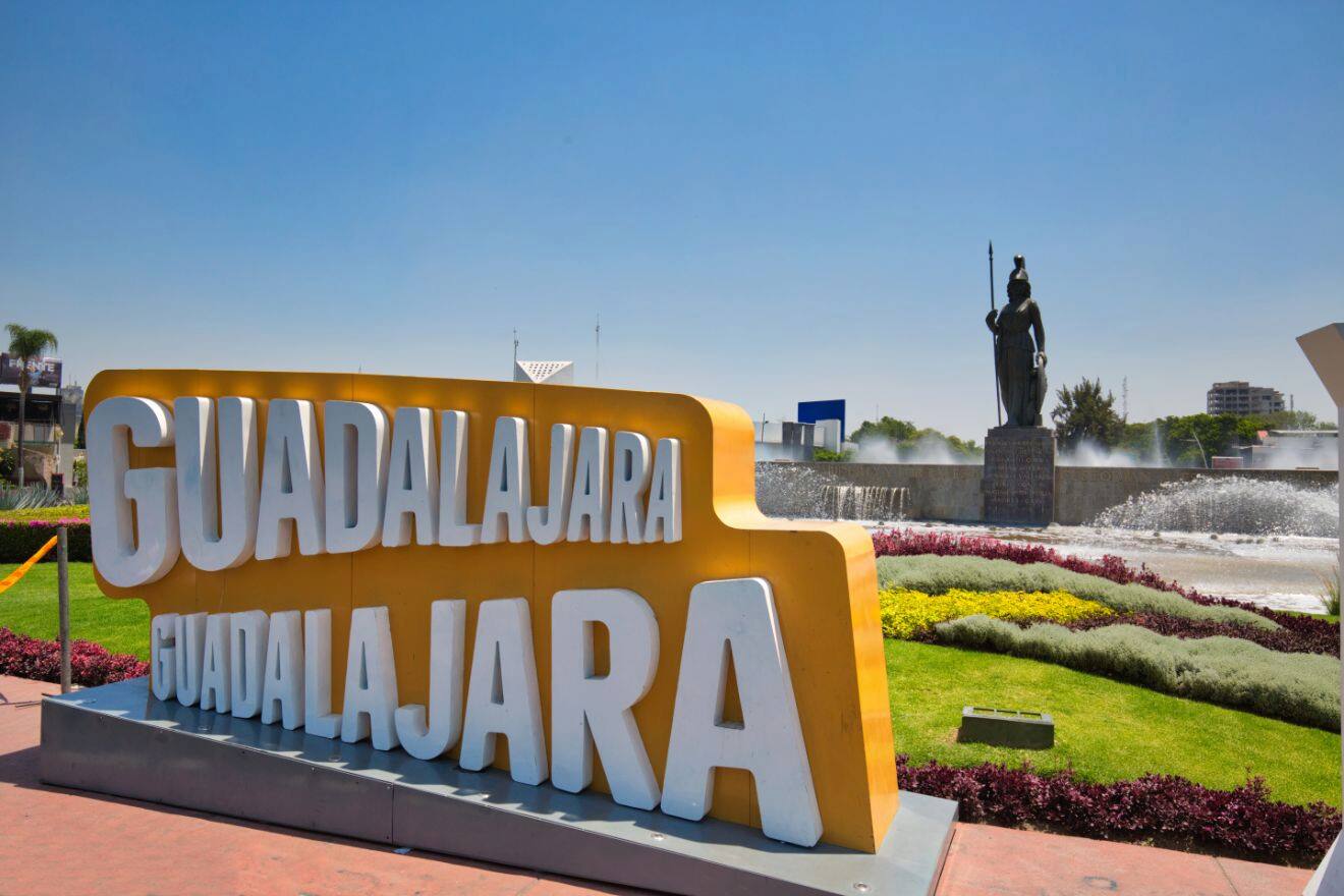 Bold 'GUADALAJARA' sign in large yellow letters set in a landscaped area with a statue and fountain, symbolizing the city's pride and heritage