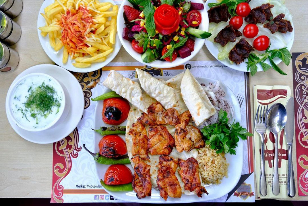 A traditional Turkish meal spread out on a table, featuring grilled meat, rice, fresh salad, fries, yogurt sauce, and flatbread, indicative of Turkey's rich culinary heritage.