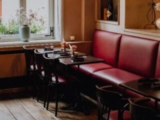 A restaurant interior with red cushioned bench seating, black chairs, dark tables, and a window with a vase of flowers.