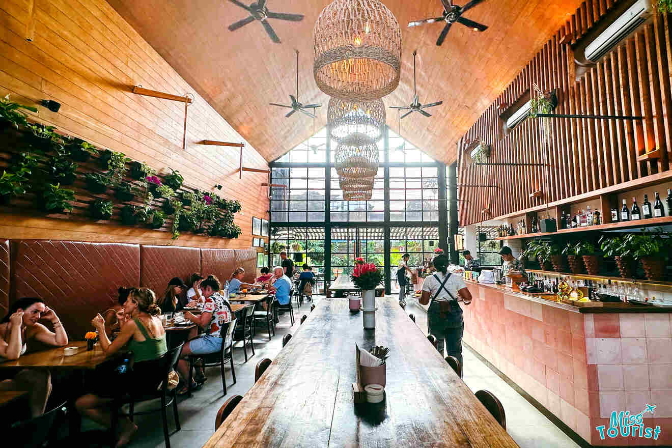 Interior of a vibrant café with a high ceiling, hanging planters, and guests dining at communal tables in Ubud