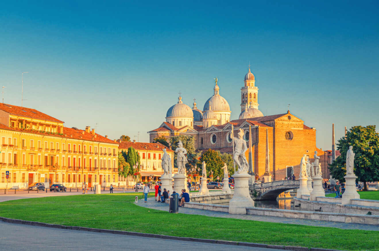 Sunset view of Prato della Valle in Padua, Italy, featuring the historic Basilica of Saint Anthony in the background with its distinctive domes and bell towers, and marble statues lining the elliptical square