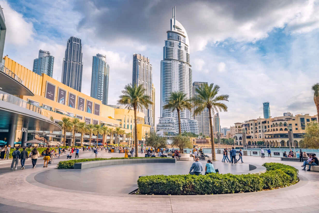 Scenic view of the bustling Downtown Dubai area featuring the Address Hotel, strolling visitors, and a modern skyline on a partly cloudy day