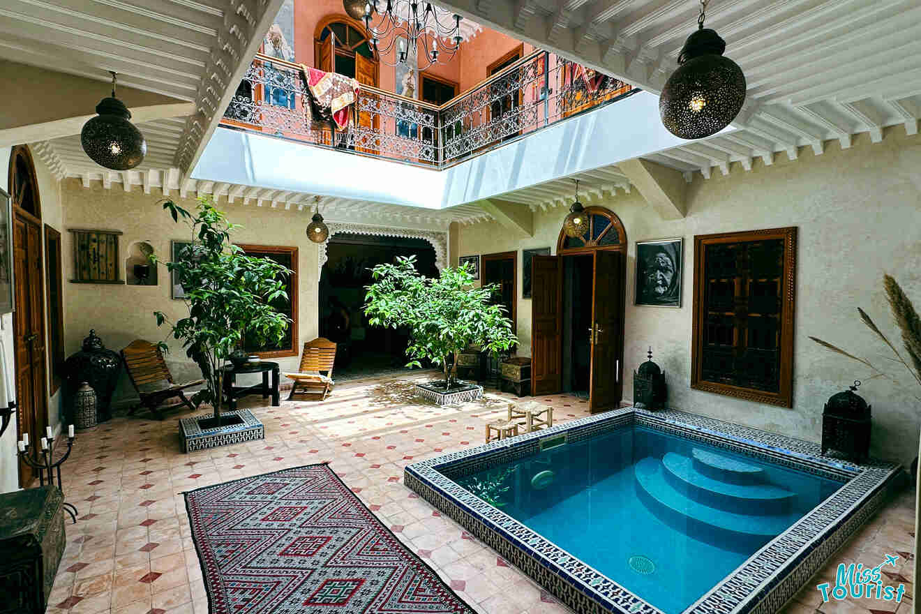 Traditional Moroccan riad courtyard with a sunlit pool, terracotta tiling, lush greenery, and cultural decorations