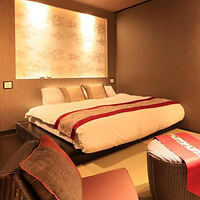 Um quarto de hotel moderno com uma cama grande, almofadas decorativas, iluminação suave e uma pequena área de estar com cadeiras e uma mesa.