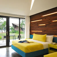 Modern bedroom featuring a bright yellow bedspread, wooden wall with inset lighting, and glass doors leading to an outdoor patio.