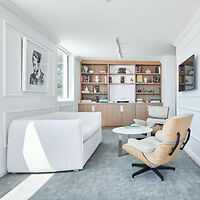 Minimalist living room with a white sofa, tan armchair, and a bookcase against white walls