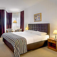Hotel room featuring a large bed with a tufted headboard, elegant striped bedcover, and classic decor