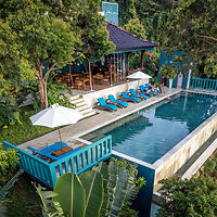 Aerial view of a luxurious poolside with loungers and a shaded seating area surrounded by lush trees.