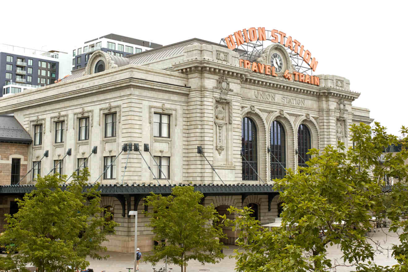 Exterior view of Union Station in Denver with 'Travel by Train' neon sign, showcasing classical architectural features